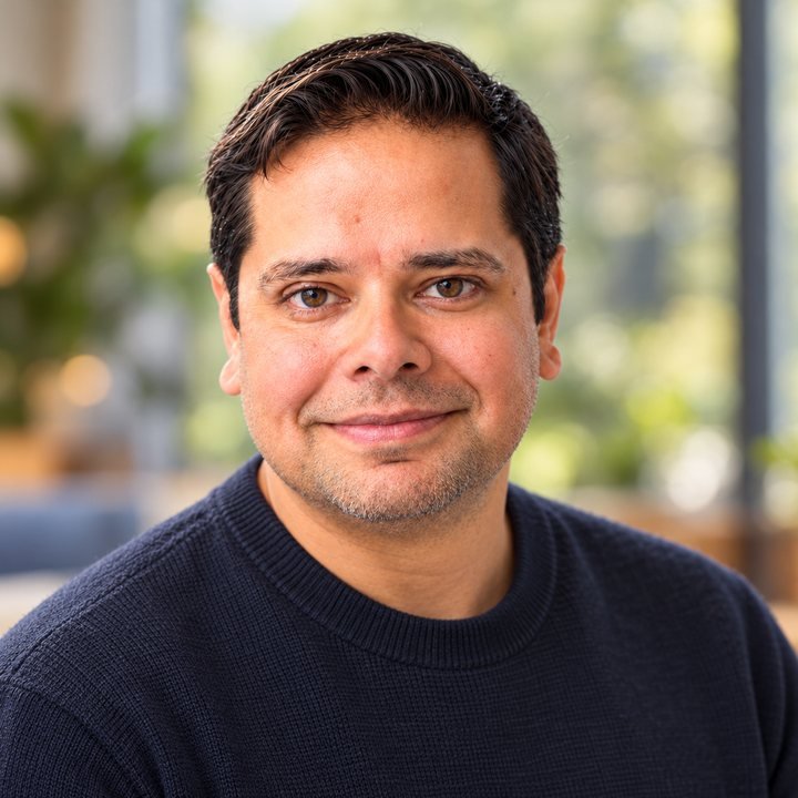 Ian Lobo smiling, in a navy sweater, with green plants softly blurred behind him